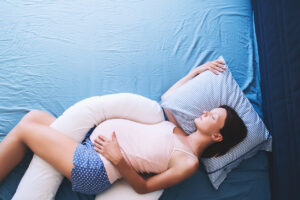 Pregnant woman lying on their side with their head on a pillow and a pregnancy pillow through their legs