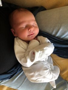 A newborn baby boy wearing a onesie looking calm and peaceful asleep